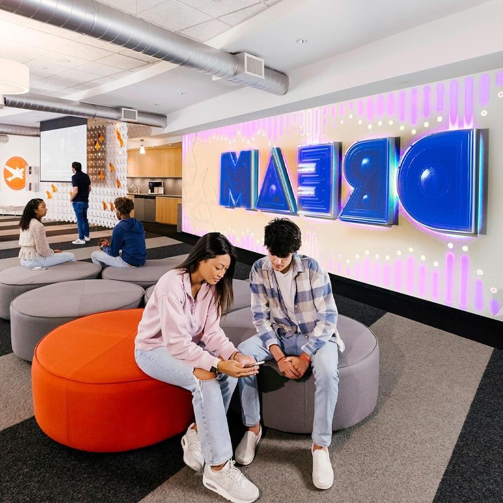 Two students sit in front of the Full Sail dream wall.